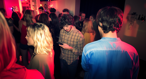 Eine Menschengruppe in Discolicht und mittendrinn ein Mann an seinem Smartphone