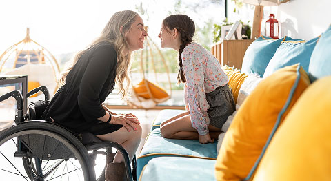Kind auf dem Sofa und Frau in Rollstuhl lächeln sich an