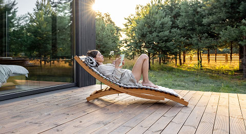 Frau liegt bei Sonnenuntergang auf einer Liege auf ihrer Terrasse und liest ein Buch