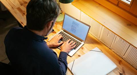 Nahaufnahme von hinten, wie Mann in blauem Hemd am Laptop tippt