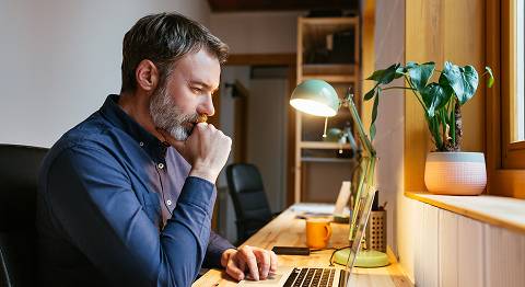 Mann in blauem Hemd sitzt grübelnd vor seinem Laptop am Schreibtisch