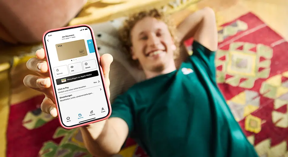 Mann liegt auf dem Boden und zeigt ein Handy mit geöffneter Banking-App und Kreditkartenübersicht