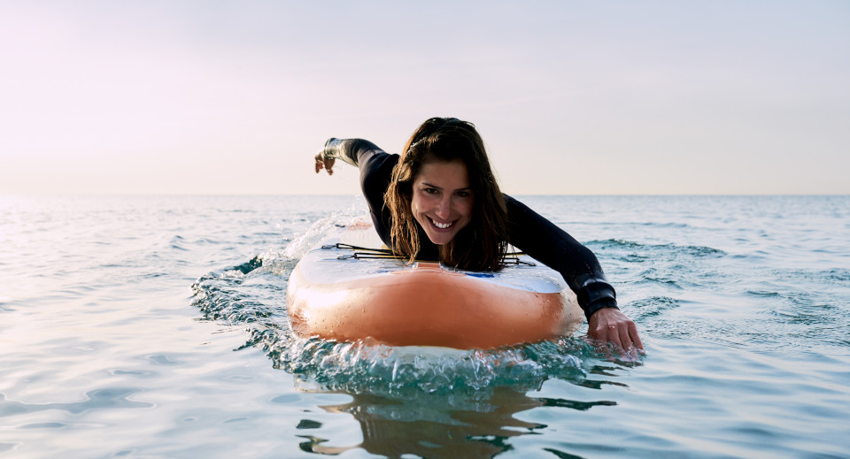 Frau in Neoprenanzug liegt auf einem Stand-Up Paddle und paddelt durchs Wasser