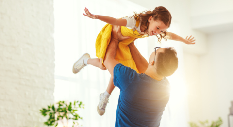 Vater hebt Tochter in die Luft und die Sonne scheint in den Raum hinein