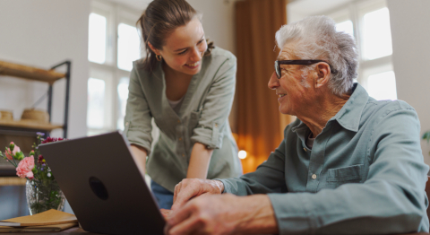 Tochter und Vater sitzen gemeinsam am Laptop und lächeln sich gegenseitig an