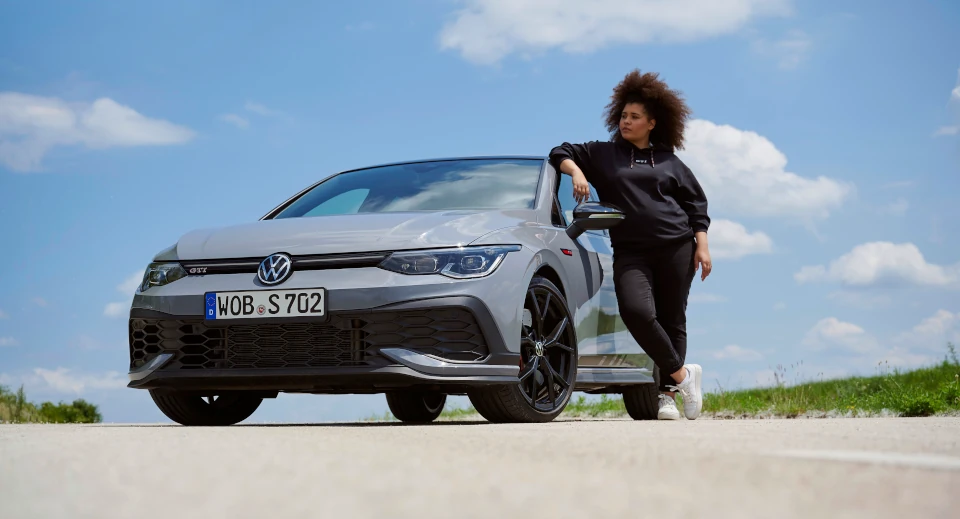 Lockige Frau steht im Freien neben grauem Volkswagen
