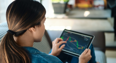 Frau mit braunen Haaren und Zopf sitzt auf Cordsofa und schaut auf ihr Tablet