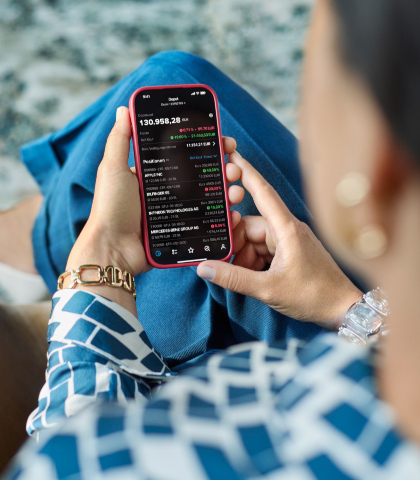 Eine Person hält ein Smartphone in der Hand und betrachtet die Übersicht eines Wertpapierdepots in einer App. Auf dem Bildschirm sind die Depotgesamtübersicht, aktuelle Werte und Kursentwicklungen sowie einzelne Aktienpositionen mit deren Kursveränderungen zu sehen. Die Werte werden in Euro sowie Prozent angezeigt.