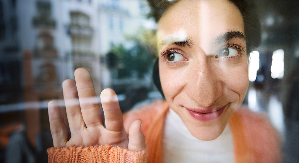 Frau schaut durch eine Glasscheibe und drückt sich die Nase platt