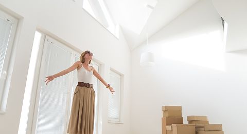 Frau mit langen blonden Haaren breitet Arme aus und steht in leerer Wohnung