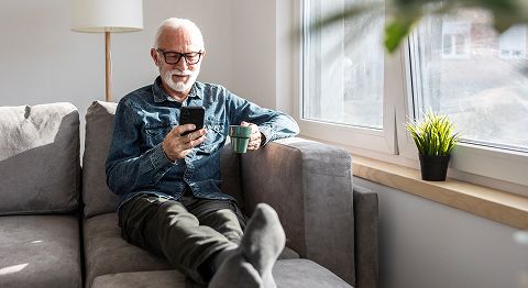 Mann kurzen grauen Haaren sitzt auf Sofa und schaut ins Handy