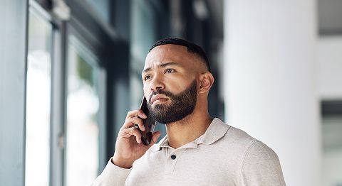 Mann mit dunklen kurzen Haaren steht am Fenster und telefoniert