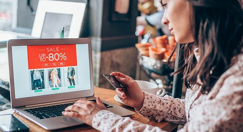 Frau mit langen braunen Haaren sitzt am Laptop und shoppt und hält Kreditkarte in der Hand