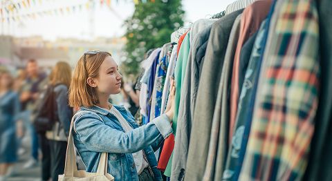 junge Frau mit langen roten Haaren steht vor Kleidungsstücken und telefoniert