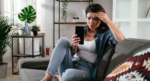 Frau sitzt auf Sofa und schaut verzweifelt in ihr Handy