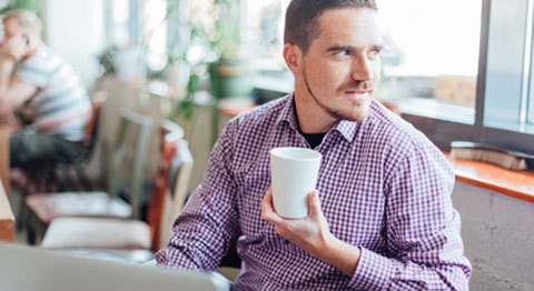 Mann in kariertem Hemd und Tasse in der Hand schaut aus dem Fenster