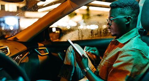 Mann mit Brille von der Seite, wie er auf einem Beifahrersitz sitzt und an seinem Tablet tippt