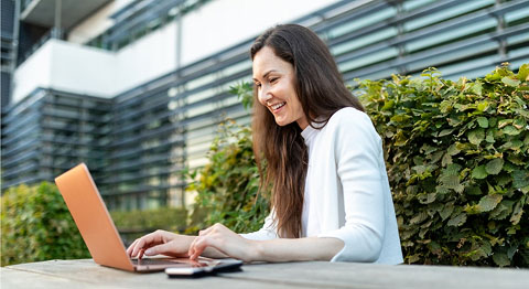 Braunhaarige Frau sitzt im Freien und arbeitet an ihrem Laptop
