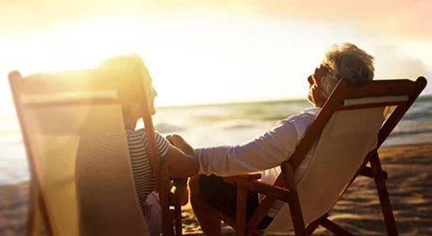 Zwei Personen sitzen bei Sonnenuntergang entspannt in einem Liegestuhl am Strand