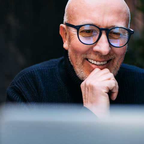 Mann mit Glatze und schwarzer Brille schaut grübelnd in seinen Laptop