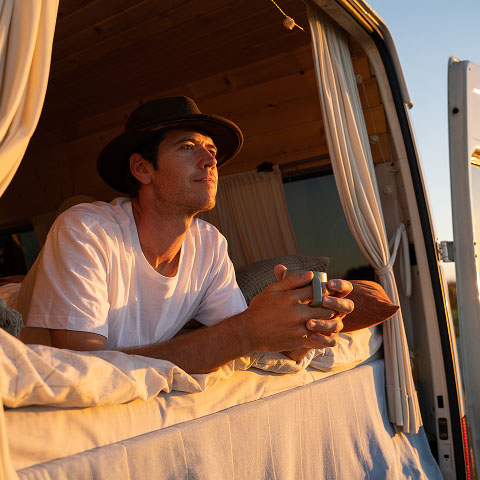 Mann mit Hut schaut auf seinem Van nach draußen