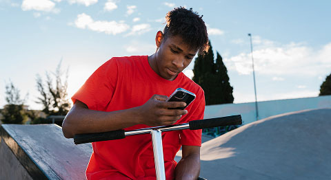 Mann in rotem T-Shirt lehnt sich auf dem Lenkrad von seinem Roller ab und schaut in sein Smartphone