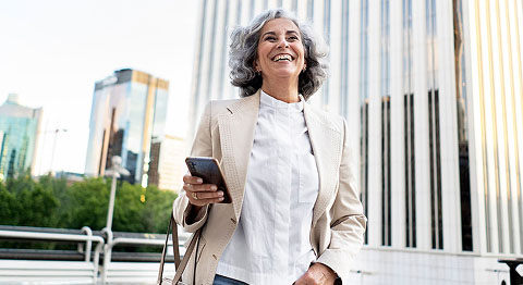 Frau mit grauen Locken in Blazer läuft durch die Straßen und lächelt