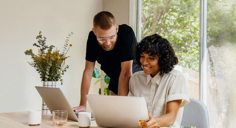 Frau und Mann sitzen im Wohnzimmer und arbeiten an zwei Laptops
