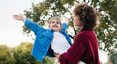 Mutter hält ihr Kinder im Freien in den Armen und beide lächeln glücklich