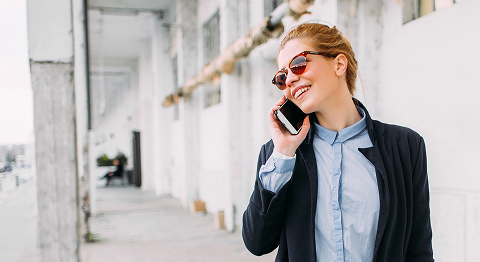 Blonde Frau in Businessklamotten mit Sonnenbrille telefoniert im Freien