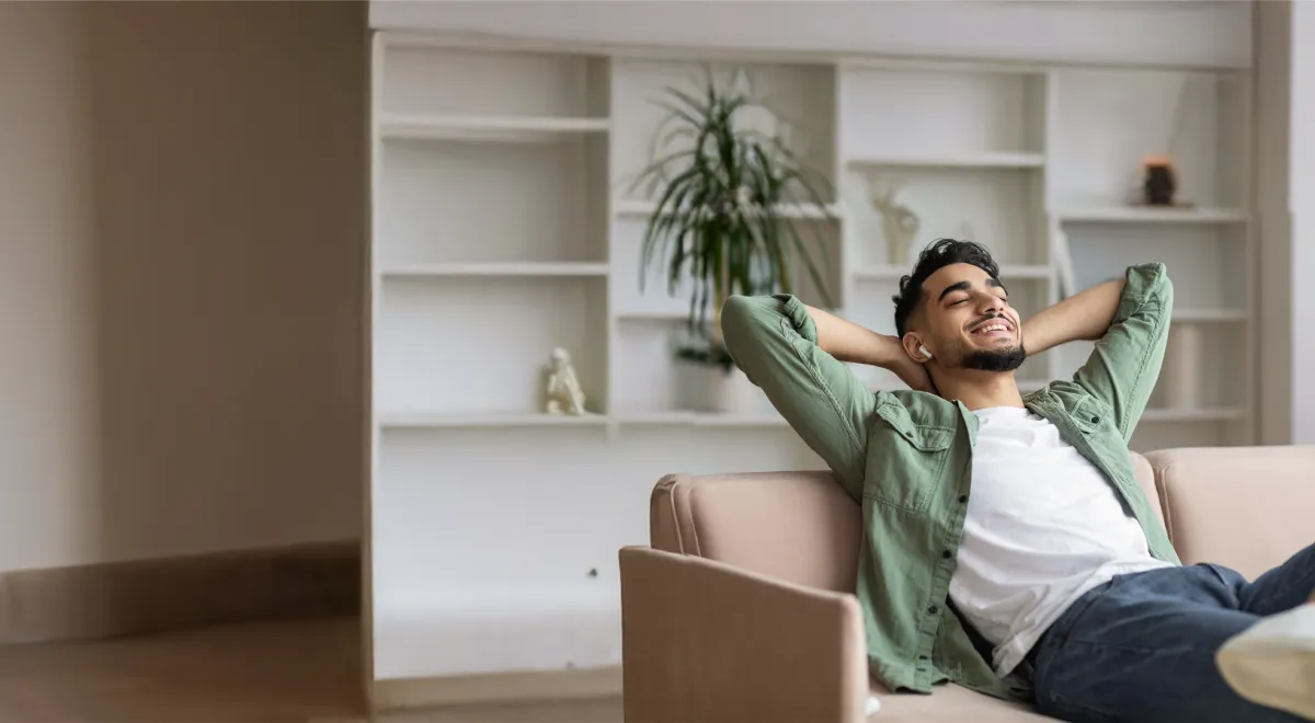Mann mit hinter dem Kopf verschränkten Armen und zufriedenen Lächeln auf einer Couch sitzend