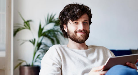 Mann mit dunkelbraunen Locken und weißem Oberteil lächelt zufrieden in die Kamera