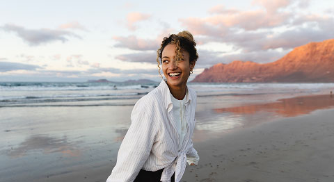 Frau mit lockigen Haaren im Zopf ist bei Sonnenuntergang am Strand