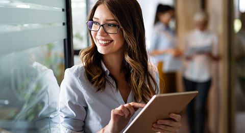 Frau mit schwarzer Brille tippt auf ihrem Tablet und schaut durch ein Fenster hindurch