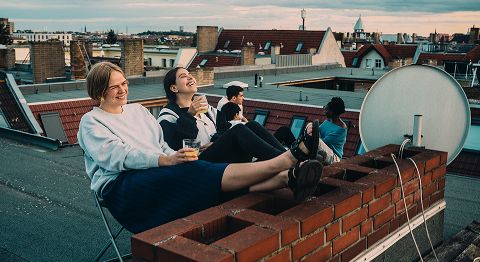 Teenager sitzen entspannt auf einer Dachterrasse mit Getränken in der Hand