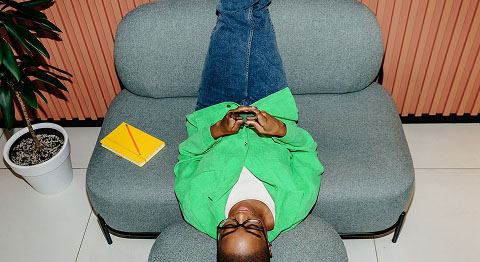 Frau in grünem Jäckchen liegt umgedreht auf dem Sofa und schaut in ihr Smartphone