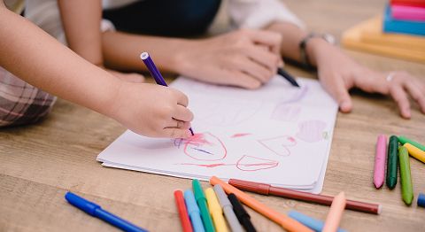 mehrere Hände malen auf einem Bild und im Vordergrund liegen mehrere Buntstifte