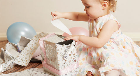 Kleinkind sitzt am Boden und packt Geschenke aus