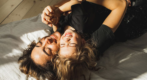 Mutter liegt zusammen mit ihrem Kind auf dem Rücken und beide lächeln