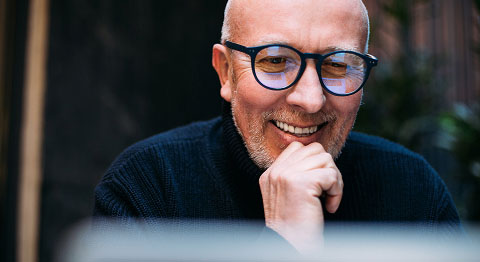 Mann mit Glatze und schwarzer Brille lächelt und sein Bildschirm spiegelt sich in den Brillengläsern