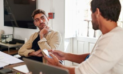 Mann im orangenen T-Shirt liegt auf der Couch mit angewinkelten Beinen und hält ein Smartphone in den Händen