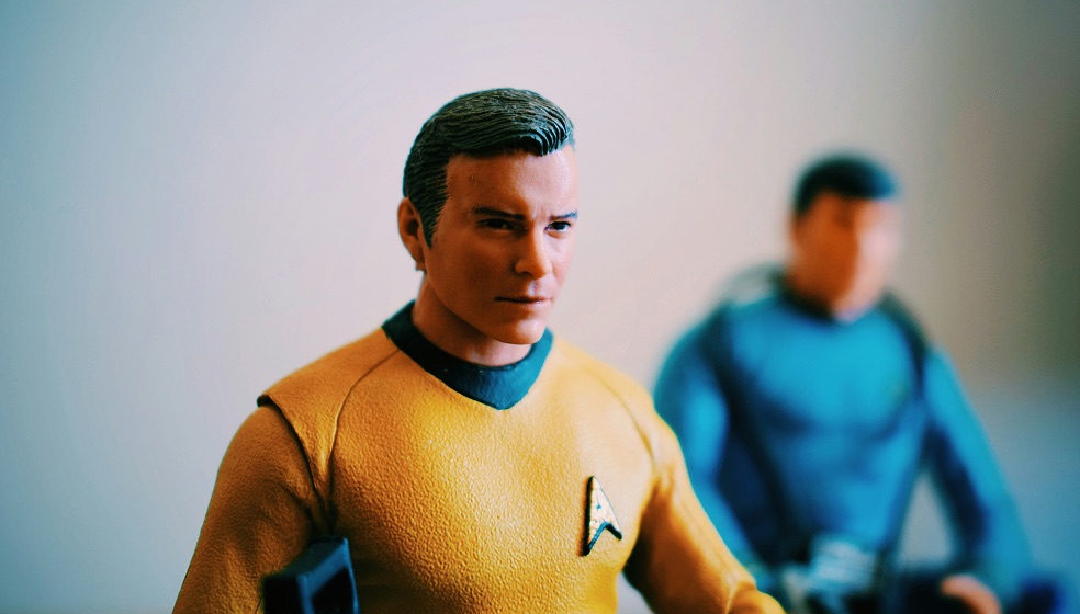 Zwei Figuren aus dem StarTrek Universum, ein braunhaariger Mann mit gelbem Pulliver ist im Vordergrund zu sehen,  und ein Mann mit dunkelbraunen Haaren und blauem Pullover im Hintergrund