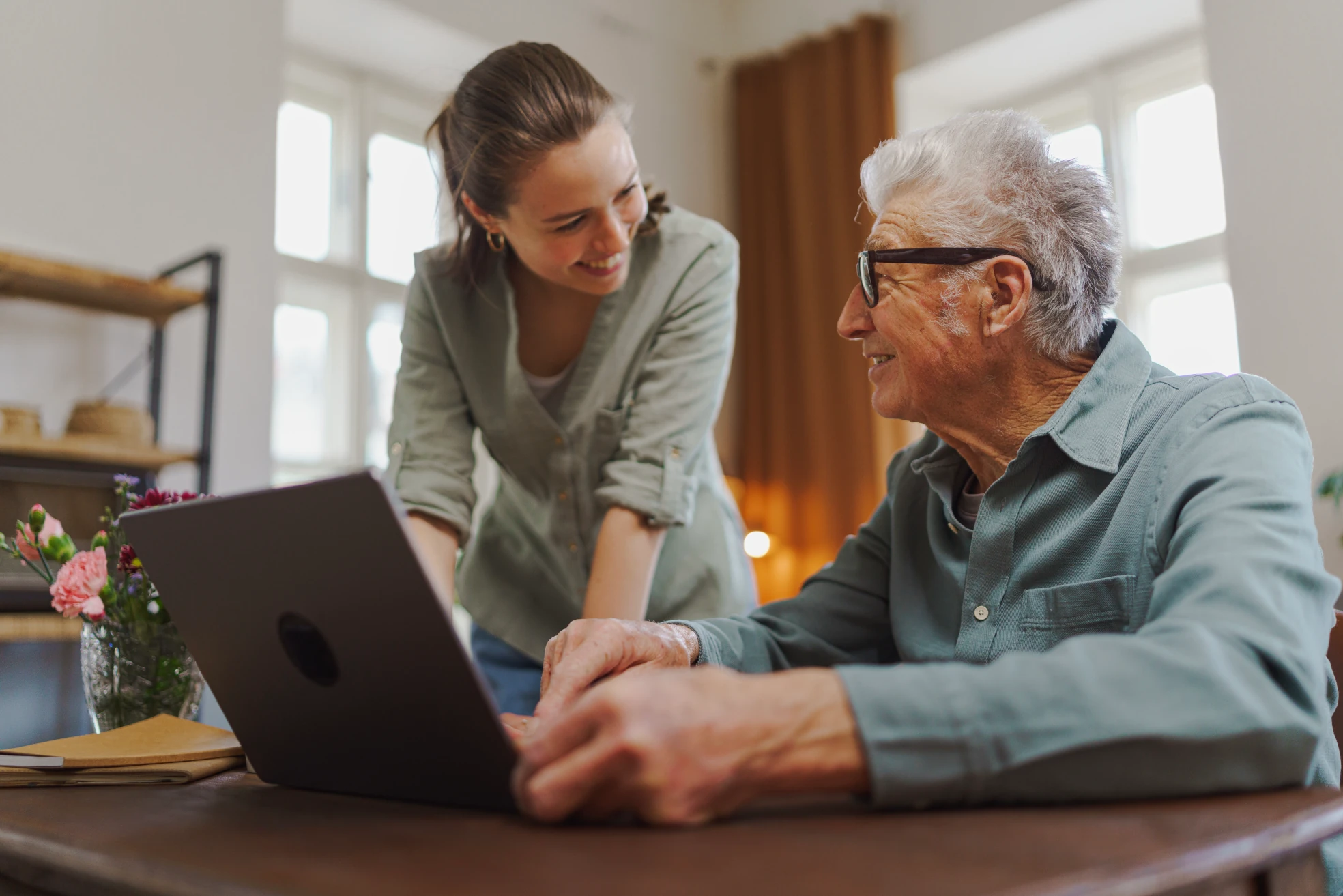 Tochter und Vater mit grauen Haaren arbeiten gemeinsam am Laptop und lächeln sich an