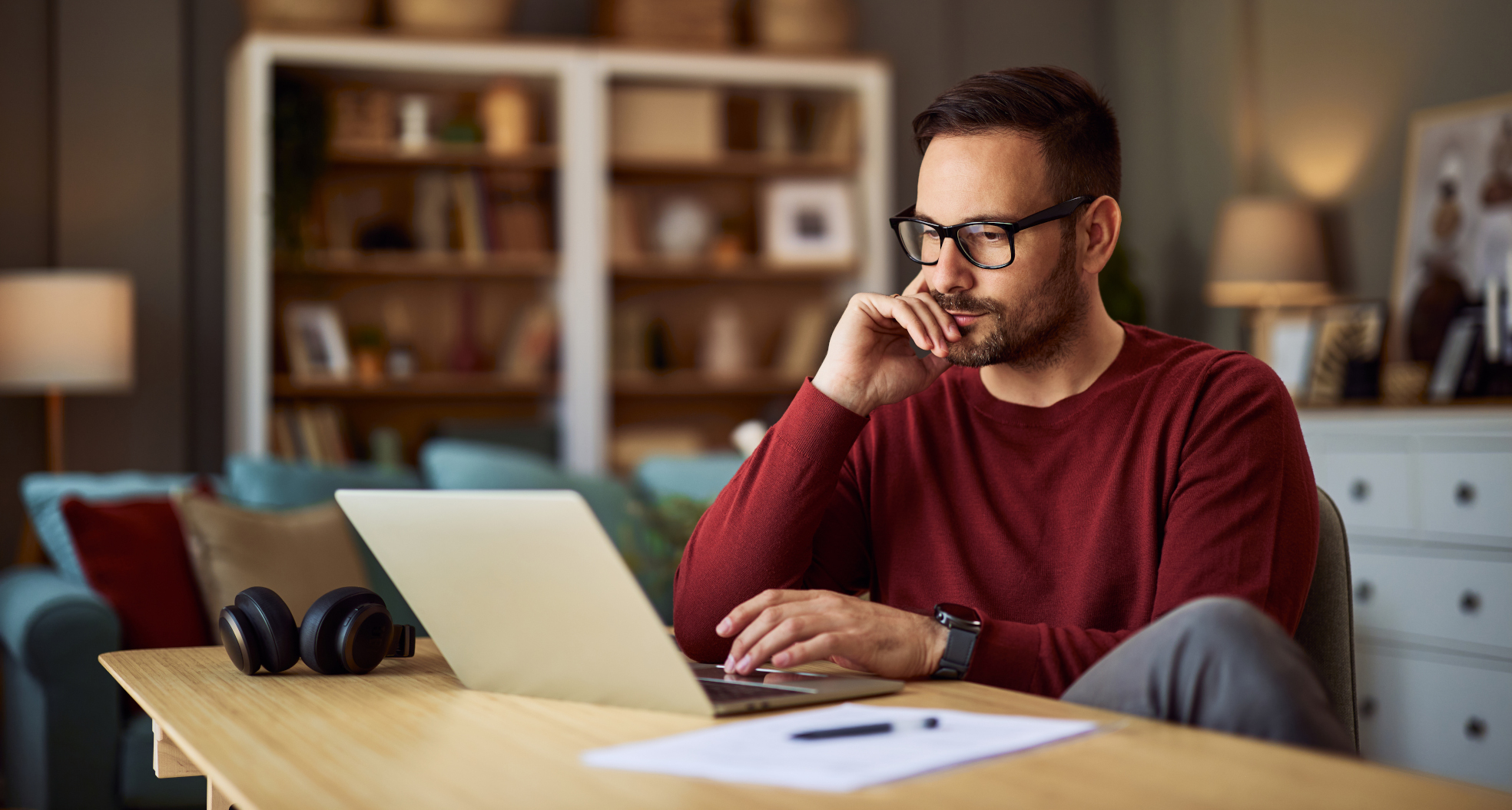 Mann in rotem Pullover sitzt am Schreibtisch vor seinem Laptop