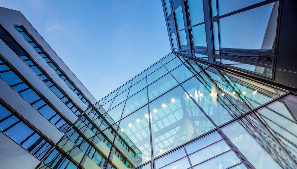 Blick auf ein komplett verglastes Bürogebäude, in dem sich der Himmel blau, grün und lila spiegelt