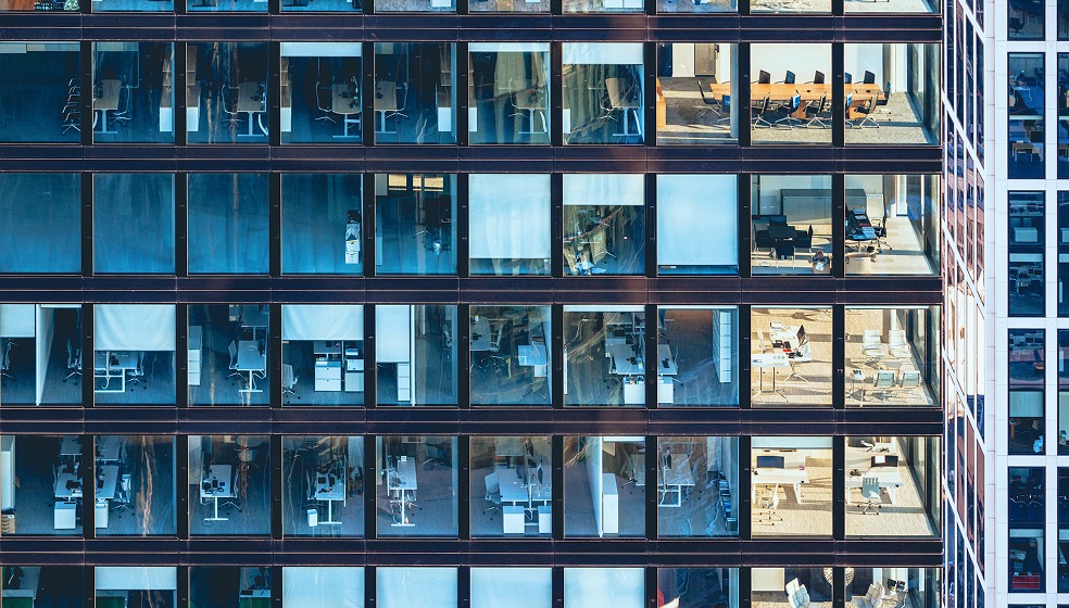 Bürogebäude mit reiner Glasfront. Wir blicken direkt von außen in viele einzelne Büros hinein. 