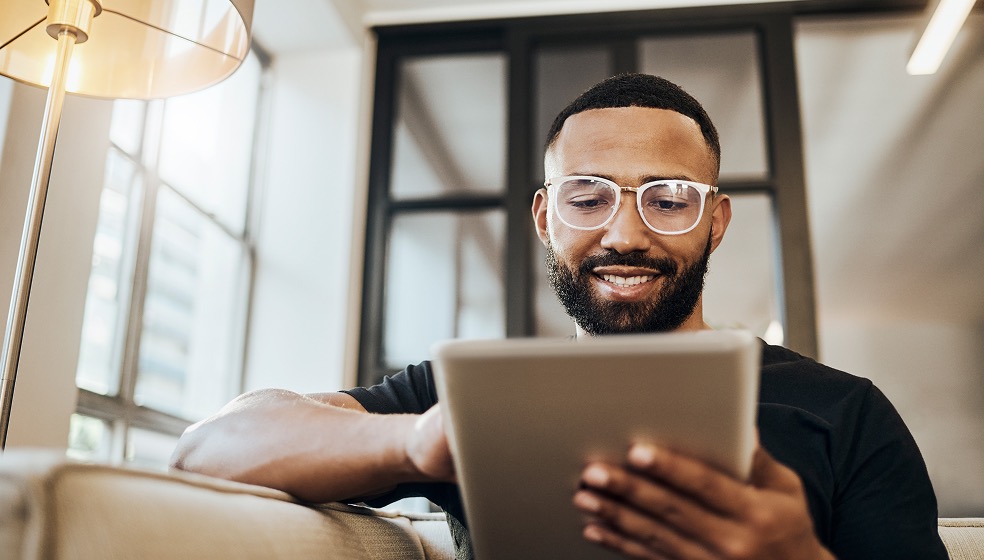 Mann mit Brille hält sein Tablet in der Hand und blickt lächelnd darauf
