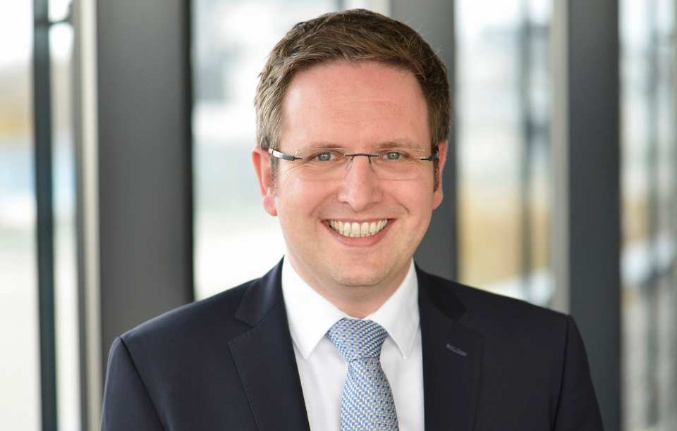 Stefan Maly, Experte für Vermögensverwaltung, hat braune Haare, eine Brille und trägt einen schwarzen Anzug mit weißem Hemd und hellblauer Krawatte