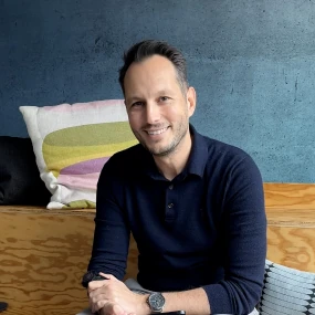 Volker Albrecht ein Mann mit dunkelbraunen Haaren sitzt auf einer Couch und lacht in die Kamera