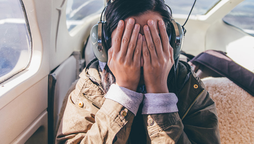 Frau sitzt mit Händen vor dem Gesicht in einem Flugzeug